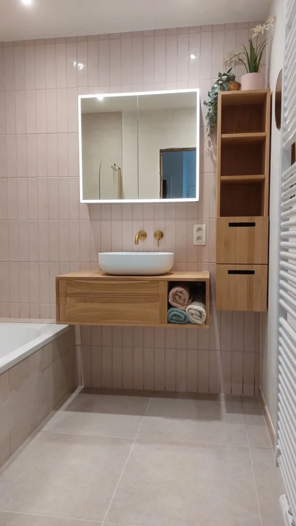 Wastafel op houten meubel met roze wandtegels en gouden kranen